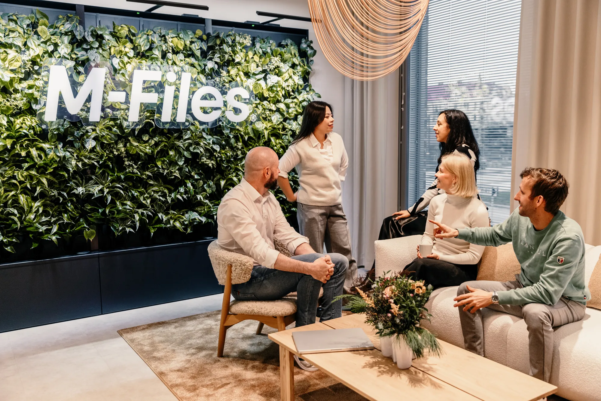 The M-Files team gathered in their office lounge, in front of the office's living plant wall